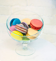 bright colored and marbled macaroons in glass vase on white brick background.
