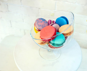 bright colored and marbled macaroons in glass vase on white brick background.