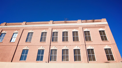 Fototapeta premium The facade of a small town mid-century designed building painted in pink against a clear blue sky in horizontal image format.