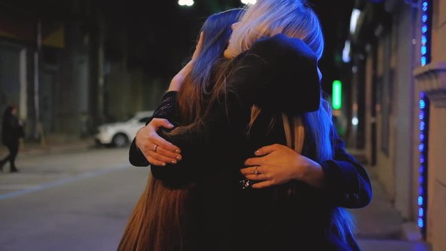 Girls night out. Friends meeting. Besties happy to see each other, hugging on the street with blur city lights.