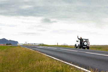 The man standing near the jeep on the side of the road and waving. The ring road number one in Iceland. Green grass on the road sides. Car trip around iceland, icelandic nature, transportation,tourism