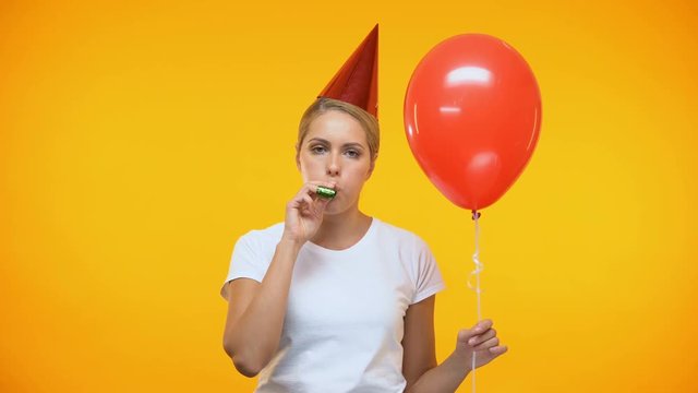 Sad adult woman blowing noisemaker holding balloon, bad mood at birthday party