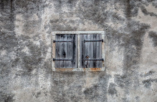 Old window with closed wooden shutters and grungy gray wall background. Shuttered window frame in ancient house