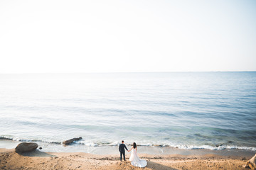Wedding couple, groom, bride with bouquet posing near sea and blue sky