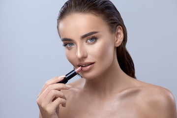 Obraz premium woman applying lipstick and looking into camera, girl with lipstick, pretty brunette applying lipstick, beautiful girl applying make-up