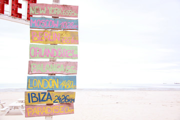 Pillar with wooden colorful signs with city names on the beach