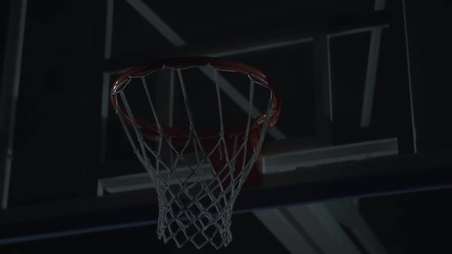 Close up image of professional basketball player making slam dunk during basketball game in dark basketball court.