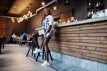 Beautiful african woman in stylish casual clothes sitting near bar counter.