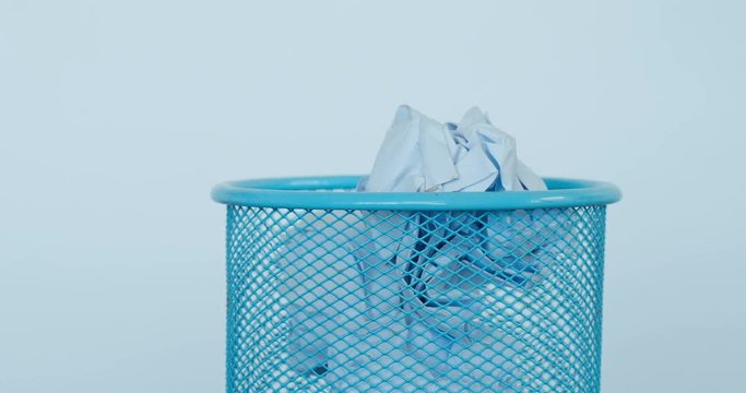 throw crumpled white useless paper into the blue trash , no idea or waste time concept