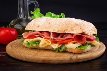 Ciabatta sandwich with lettuce , prosciutto and  cheese on wooden board