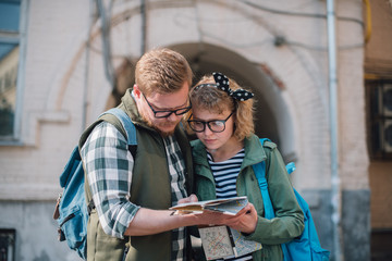 A young couple of tourists are looking for a road with a map in their hands in the city.