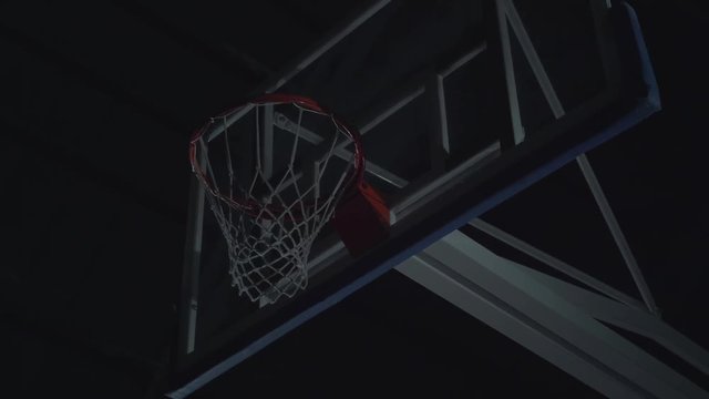 Close-up image of professional basketball player making slam dunk during basketball game in floodlight basketball court.
