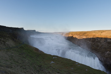 Landscape with meadow and waterfall on foreground, and mountains on background, on an early evening summer day, Gullfoss waterfall, canyon of the glacial river Hvítá, Colour Photo, Iceland