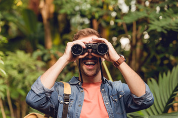 adult happy traveler looking through binoculars in tropical green forest