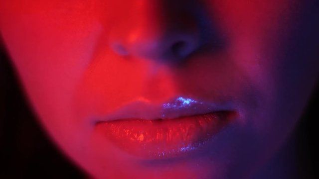 Closeup shoot of pretty female lips with red neon light and bokeh background at nightclub