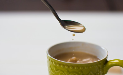  A cup of tea with milk. Mixing tea with a spoon. Spoon of tea. Green cup. A cup of coffee