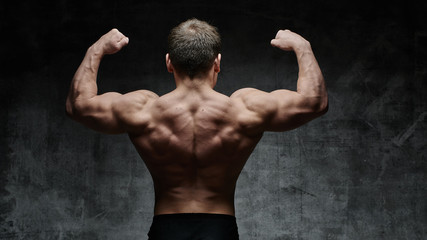 Sexy bodybuilder man posing from the back on dark background. Handsome pumped male body isolated...