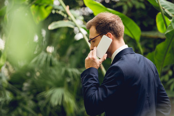 businessman in suit and glasses talking on smartphone in greenhouse