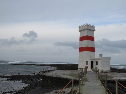 Lighthouse on a rough coast-line surrounded by sea and sky, photo taken from gangway leading to lighthouse