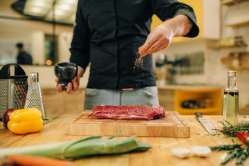 Male person marinating raw meat on wooden board