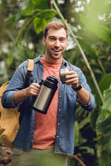 Naklejka premium selective focus of happy traveler with backpack opening thermos in tropical forest