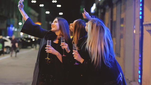 Girls night out party. Female friends taking selfie, standing with champagne on the street with blur city lights.