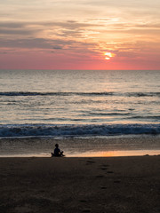 Silhouette of an indefinite person in lotus position on a sea sandy beach during a beautiful sunset. Meditation during sunset. A child is meditating on the evening sea beach.