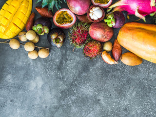 Various fresh Thai fruits - rambutan, mango, mangosteen, longan, papaya, dragon fruit, sapodilla, passion fruit, salak, pineapple on a wooden tray and a gray background. Top view. Copy space