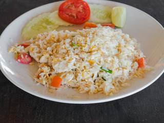 Dish of Asian cuisine - fried white rice with egg, chicken meat and vegetables on a white plate on the wood table in a Thai restaurant