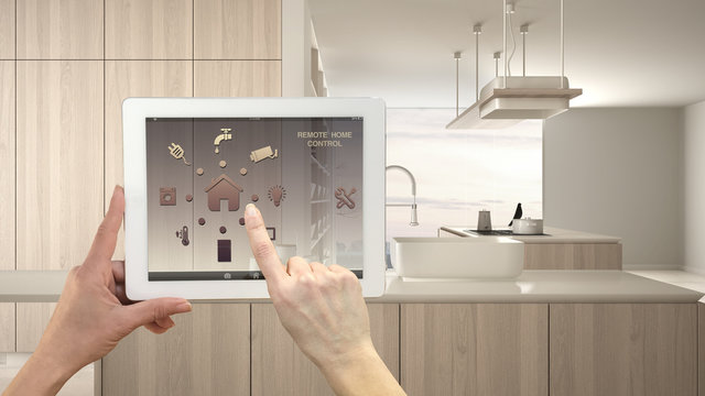 Smart remote home control system on a digital tablet. Device with app icons. Modern kitchen with wooden details in contemporary apartment background, architecture interior design