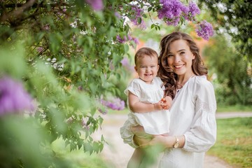 Beautiful young mother and little cute daughter are happy near the lilac. Portrait of mom and...