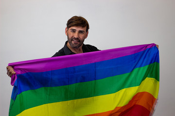 Portrait of handsome young man with gay pride movement LGBT Rainbow flag and brown hair making an...