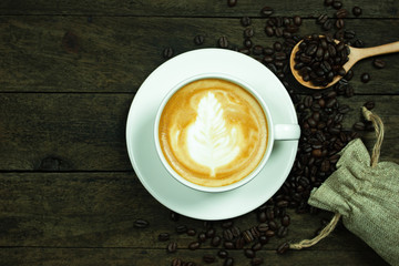 latte art in a cup and coffee beans on wood table
