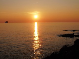 Fototapeta premium Genova, Italy - 03/15/2019: An amazing caption of the sunset in spring days over the sea of Genova with beautiful red and blue sky, some amazing clouds in the background and old rocks over the sea.