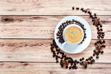 Top view of a cup of hot coffee on wooden rustic table with spilled coffee beans and anise.
