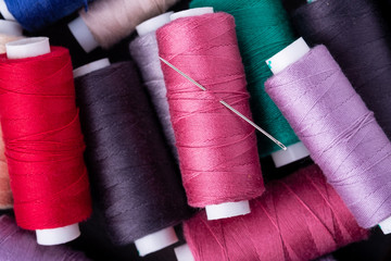 Top view close up of scattered colorful cotton thread coils with needle