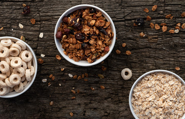 A variety of dry cereal in white bowls on a wooden background, top view. Uncooked oatmeal, granola and cereal.