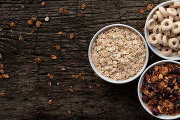 A variety of dry cereal in white bowls on a wooden background, top view. Uncooked oatmeal, granola and cereal.