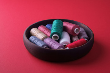Angle view of scattered colorful cotton thread coils in wooden plate red background