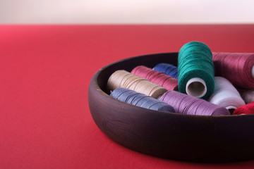 Angle view of scattered colorful cotton thread coils in wooden plate red background