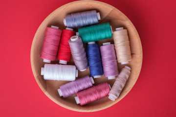 Top view of scattered colorful cotton thread coils in wooden plate red background