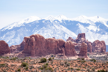Compressed view of natural sandstone rock formations in front of snow capped peaks of the La Sal Mountains in Arches National Park. 