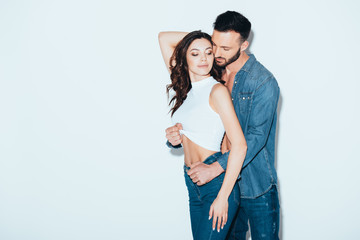 Naklejka premium bearded man in jeans undressing girlfriend on grey