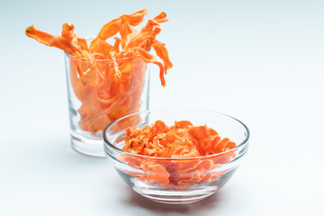 Transparent bowl and glass with homemade healthy carrot chips on gentle blue background.  