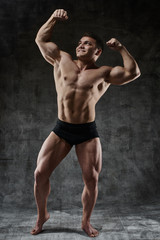 Sexy bodybuilder man posing in full growth on dark background in black shorts. Handsome pumped male...