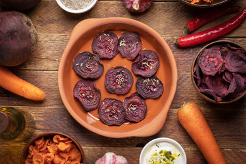 Plate and cups with healthy homemade  vegetable chips and  whole vegetables on wooden background.  