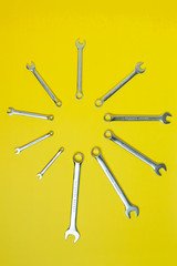 wrenches on a yellow background are arranged in the form of a clock face. The concept of time and repair