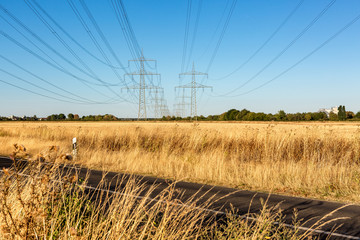 Obraz premium Überlandleitung über eine asphaltierte Straße, die von goldenen Feldern umgeben ist