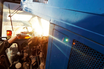 Farmer mechanic repairing blue tractor engine. Repair agricultural technology at sunset. Refueling tractor.