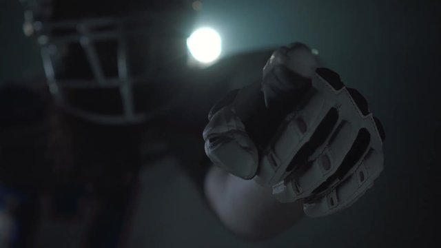 Close up portrait of american football player in sports equipment and helmet pointing his finger in camera on dark background with spotlight. Front view